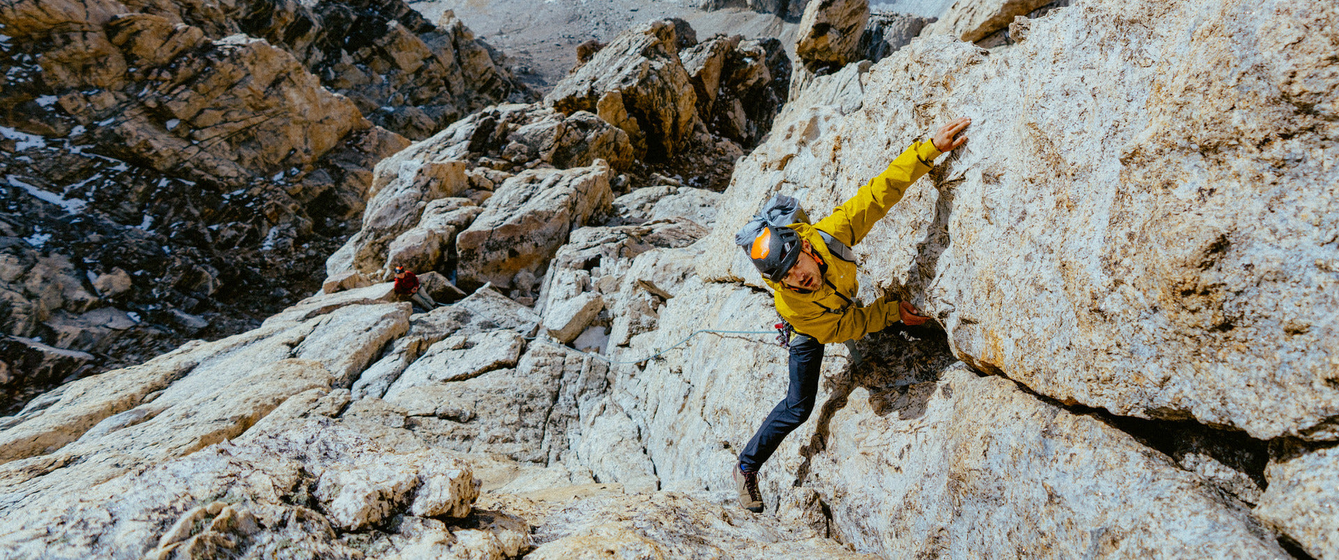 Person climbing a rocky mountain face wearing a yellow jacket.